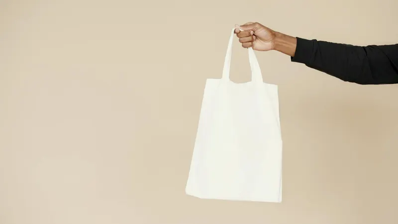 Stylish and simple white tote bag held by a hand against a neutral background, perfect for branding or eco-friendly themes.