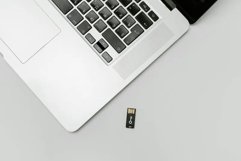 Minimalist flat lay of a laptop with USB drive over a gray background, showcasing technology essentials.